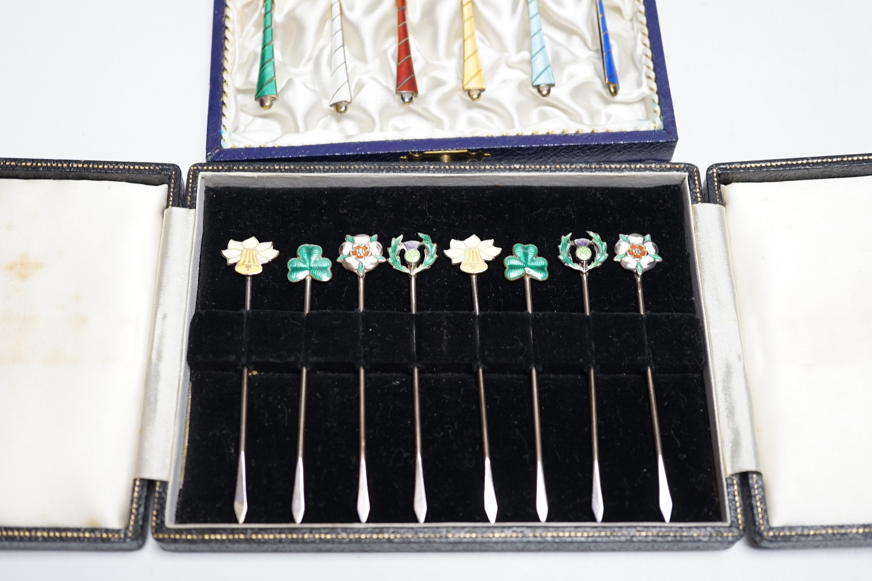 A cased set of six Danish gilt sterling and polychrome enamelled coffee spoons and a cased set of eight enamelled white metal cocktail sticks, stamped 'silver', the terminals decorated with the floral emblem of the count